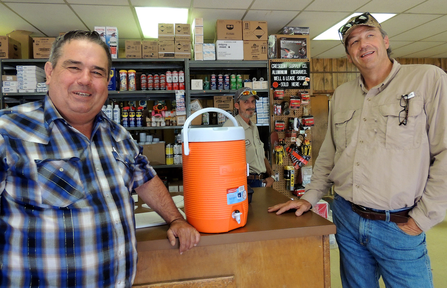 The proverbial oilfield water can is worth a laugh amid the banter at Crescent Supply Co. in Abilene. "If you ever drink out of that water can, it's like cocaine," said customer Derrell Riggan, right, referring to the addictive nature of working in the oil industry. "You can't get off of it," said Scott Tarpley, Crescent manager. "You're done." Behind the counter is Rickey Weaver, assistant manager. Riggan owns DWR Oil Co. in Merkel. PHOTO BY HANABA MUNN WELCH